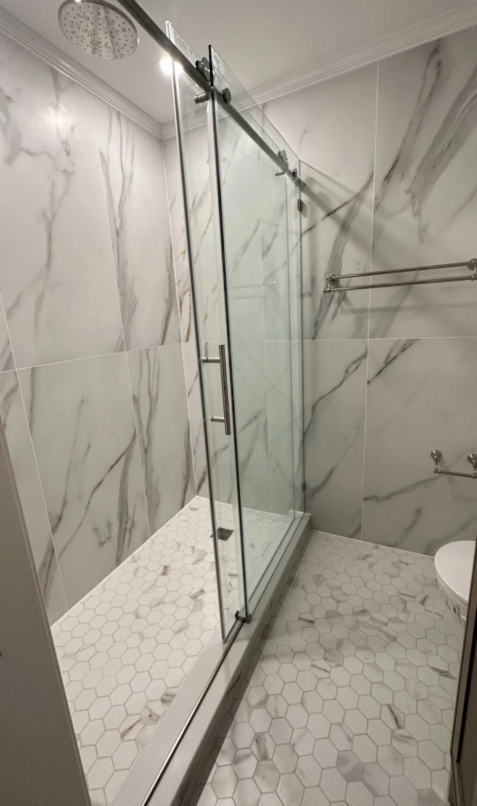 HKB glass shower with veined tile and a hexagonal tile floor